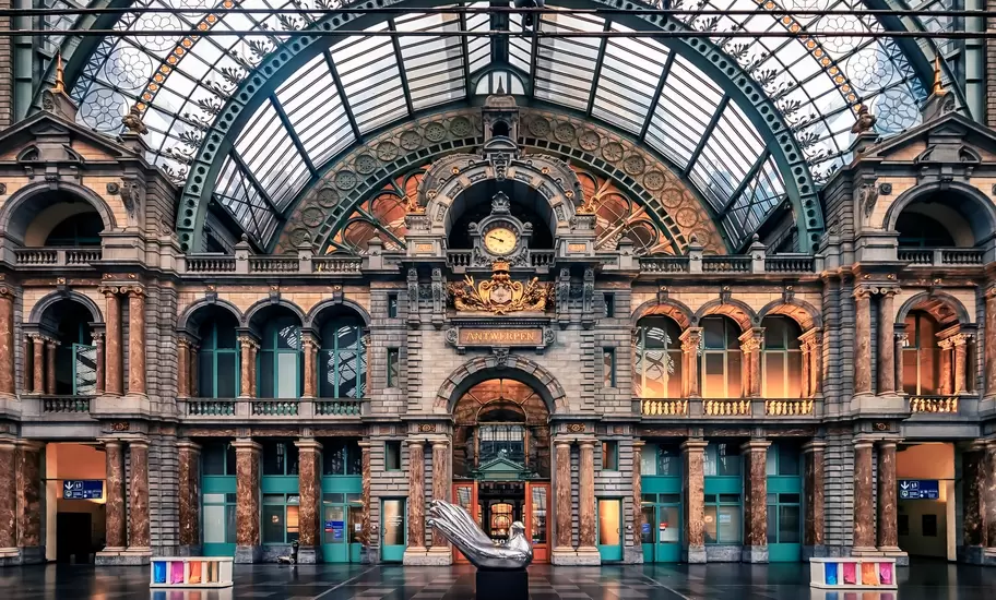 The interior of a grand station with a clock, glass ceiling and ornate windows