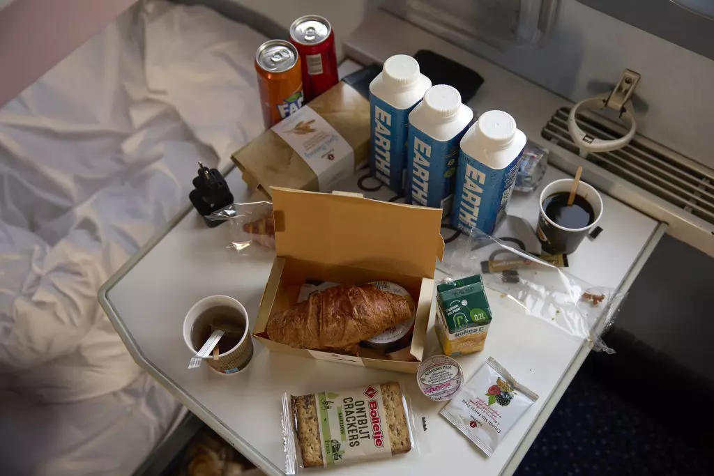 Train table with coffee, bottled drinks, and food items, including a croissant and crackers.