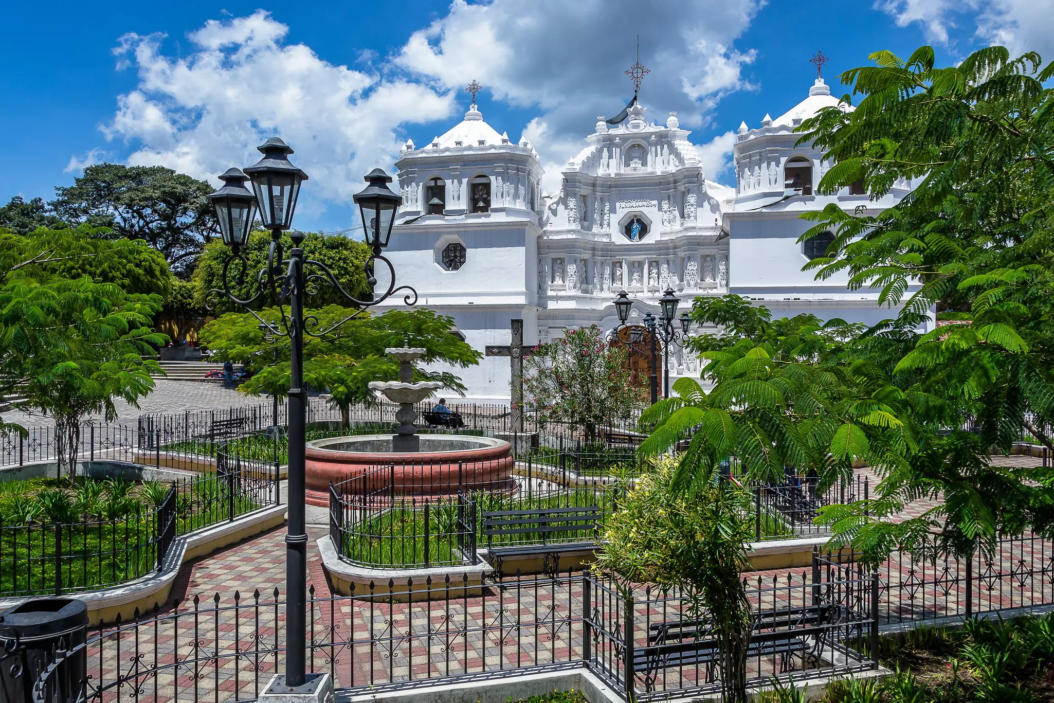 An ornate white church with a iron-fenced brick courtyard in front on a bright, sunny day.
