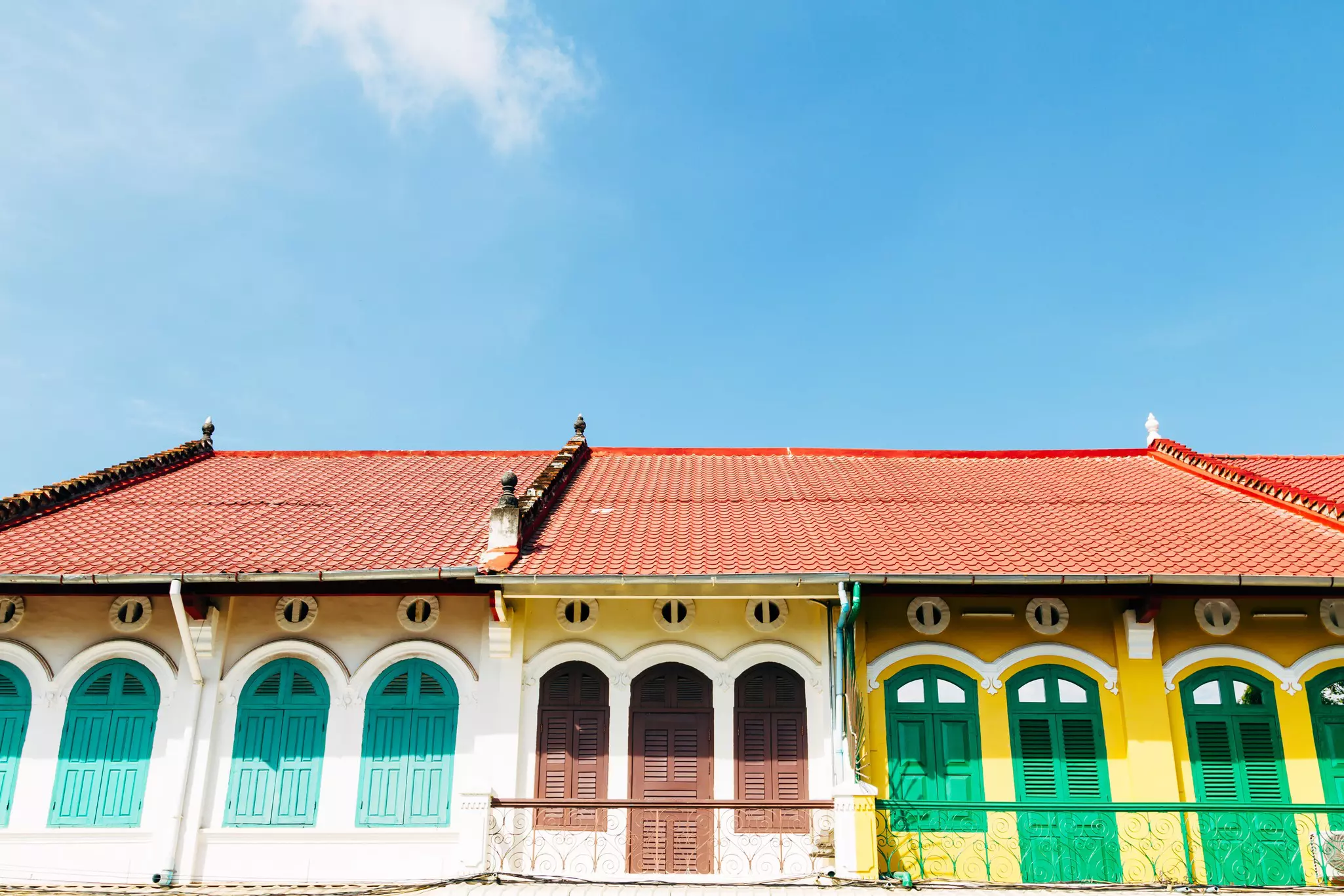The top floor of shops in Battambang, Cambodia, are painted in yellow and white, with shutters in green, brown and turquoise, under red tiled roofs.