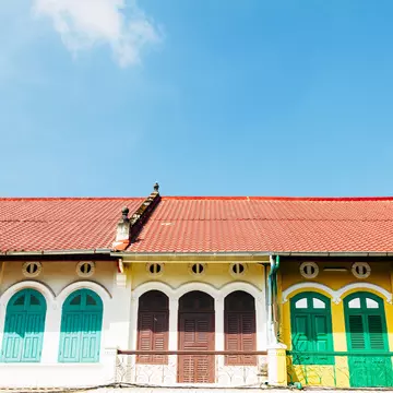 The top floor of shops in Battambang, Cambodia, are painted in yellow and white, with shutters in green, brown and turquoise, under red tiled roofs.