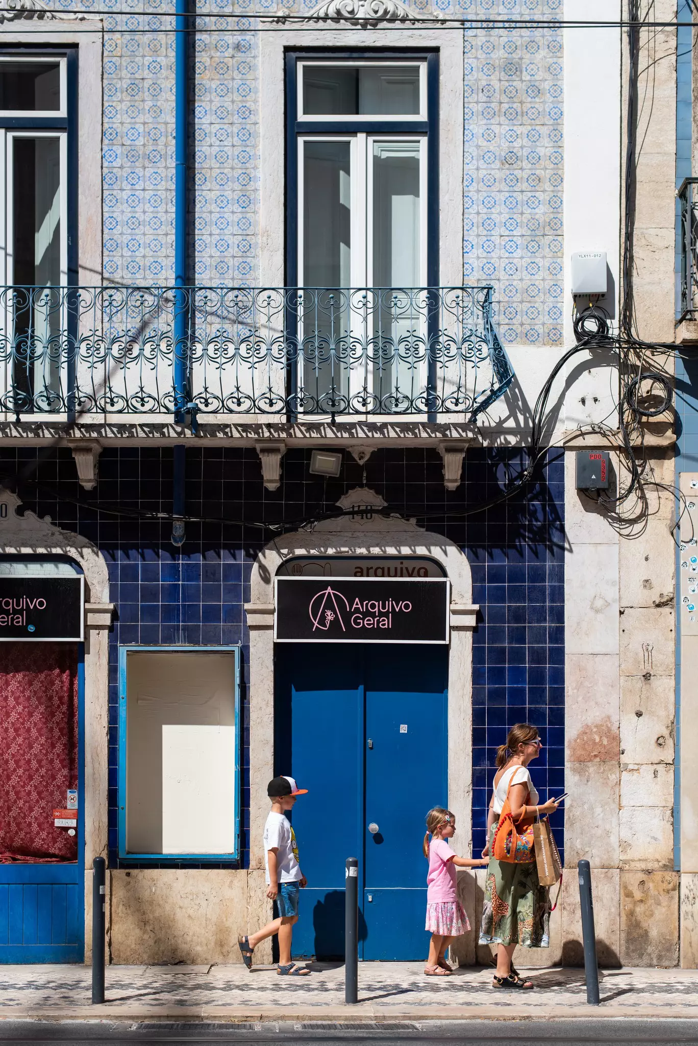 A family visiting Lisbon, Portugal passed doorways with tiled walls. The woman holds her childs hand.