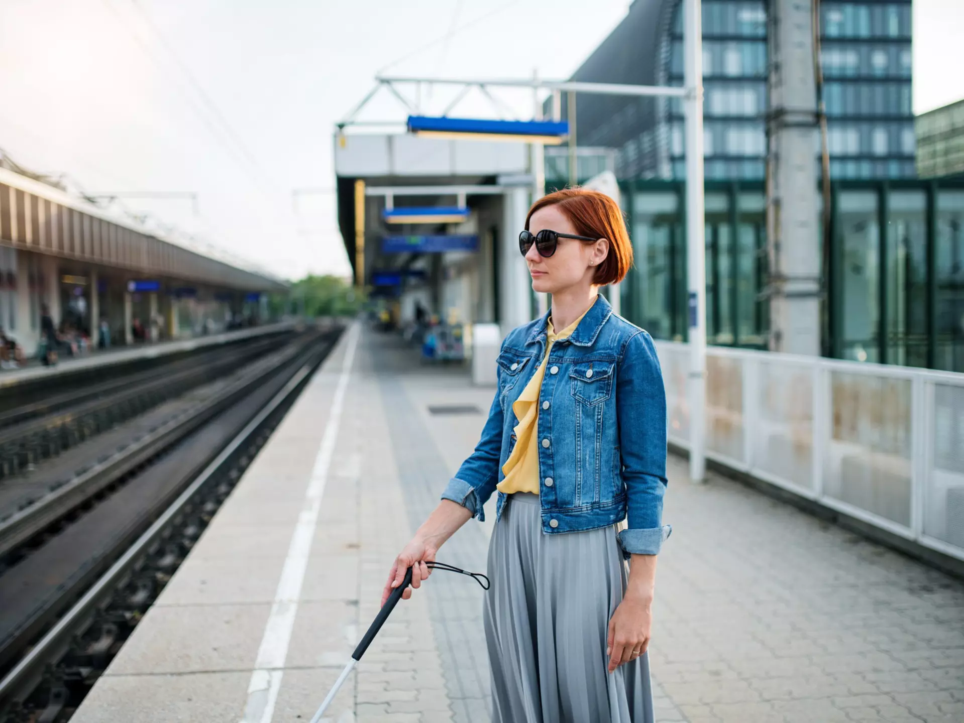 portrait of a blind woman with a white cane standing outside, waiting for public transport in summer.