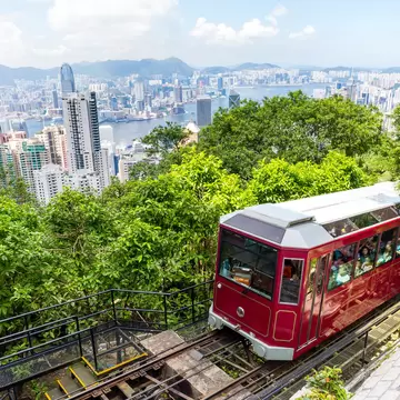 Hong Kong's Peak Tram, a red train car going up an incline with Hong Kong skyline views in he background