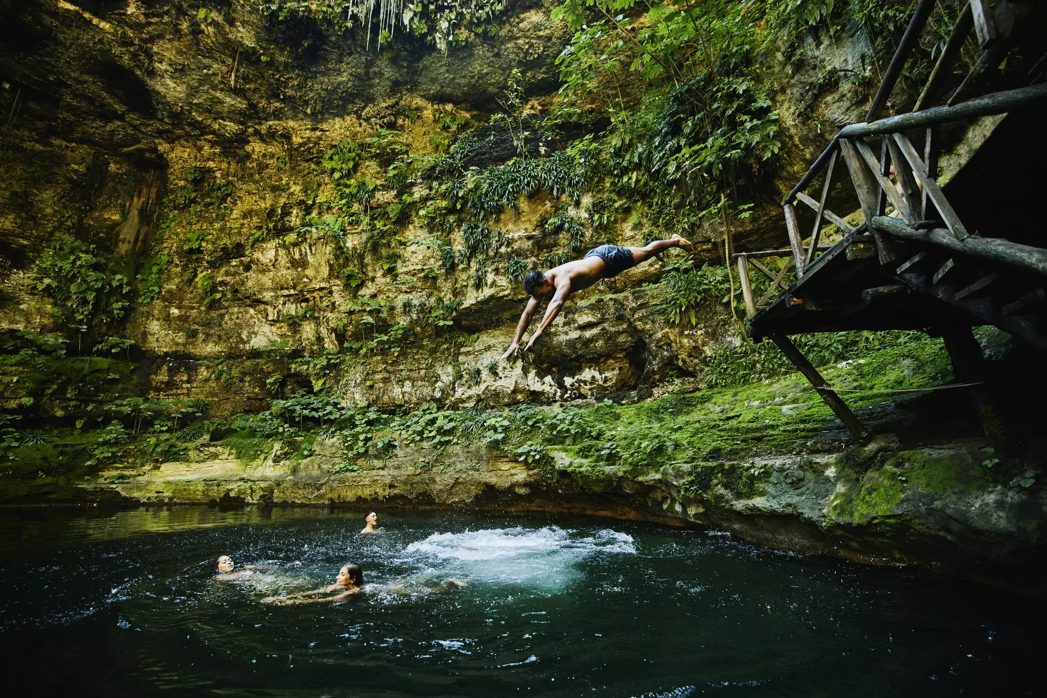 Wide shot of man diving into cenote with friends.