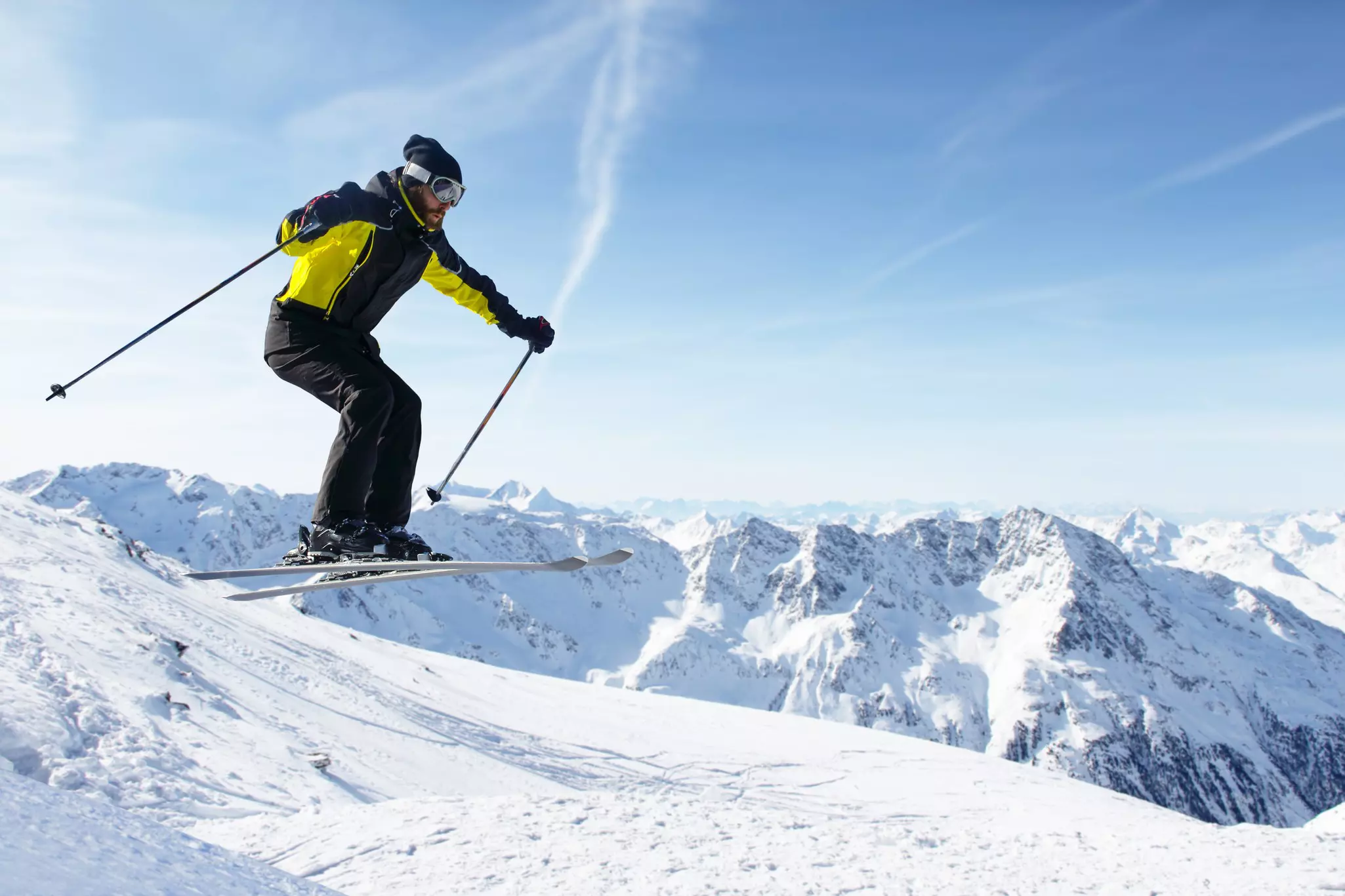 A skier jumping with alpine high mountains behind him