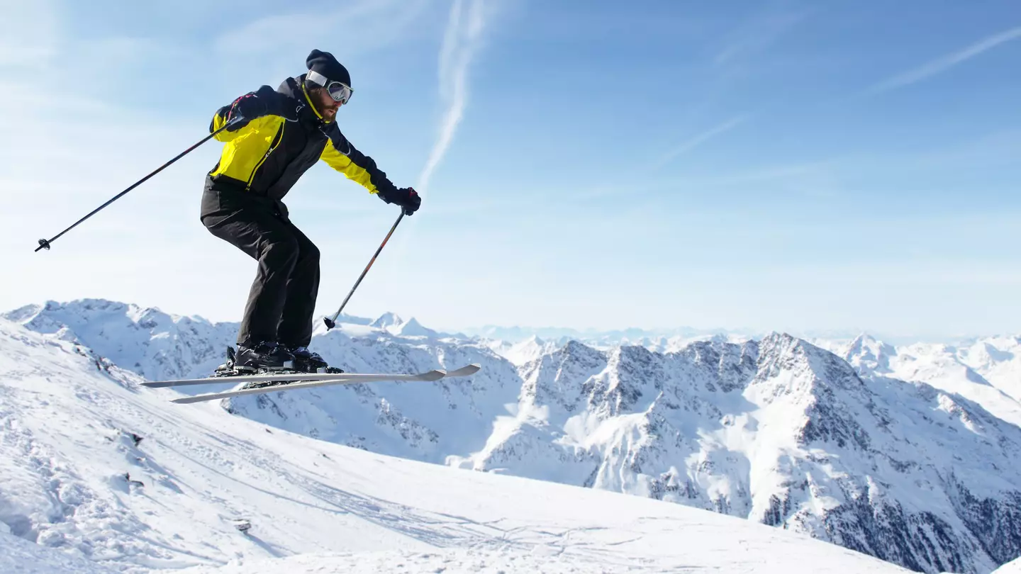 A skier jumping with alpine high mountains behind him