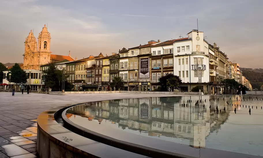 Braga's Praça da República at dusk, with the Congregados church towers and Turismo building reflected in a fountain pool