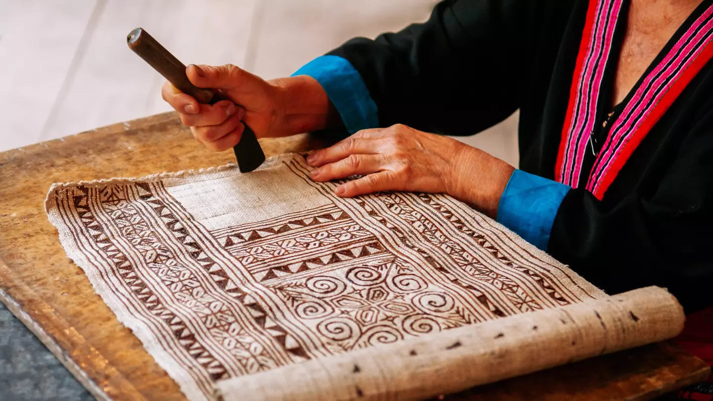A person works on a batik textile with a geometric design.