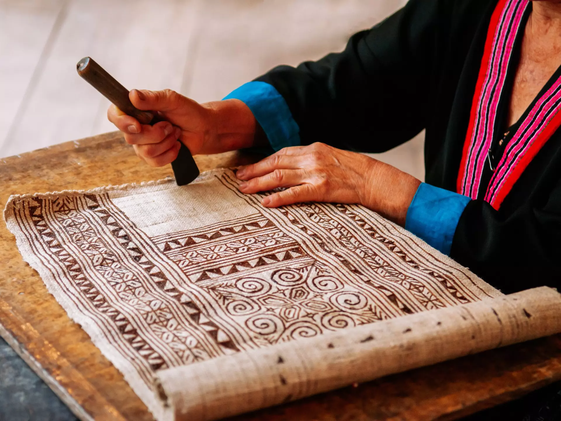 A person works on a batik textile with a geometric design.