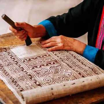 A person works on a batik textile with a geometric design.