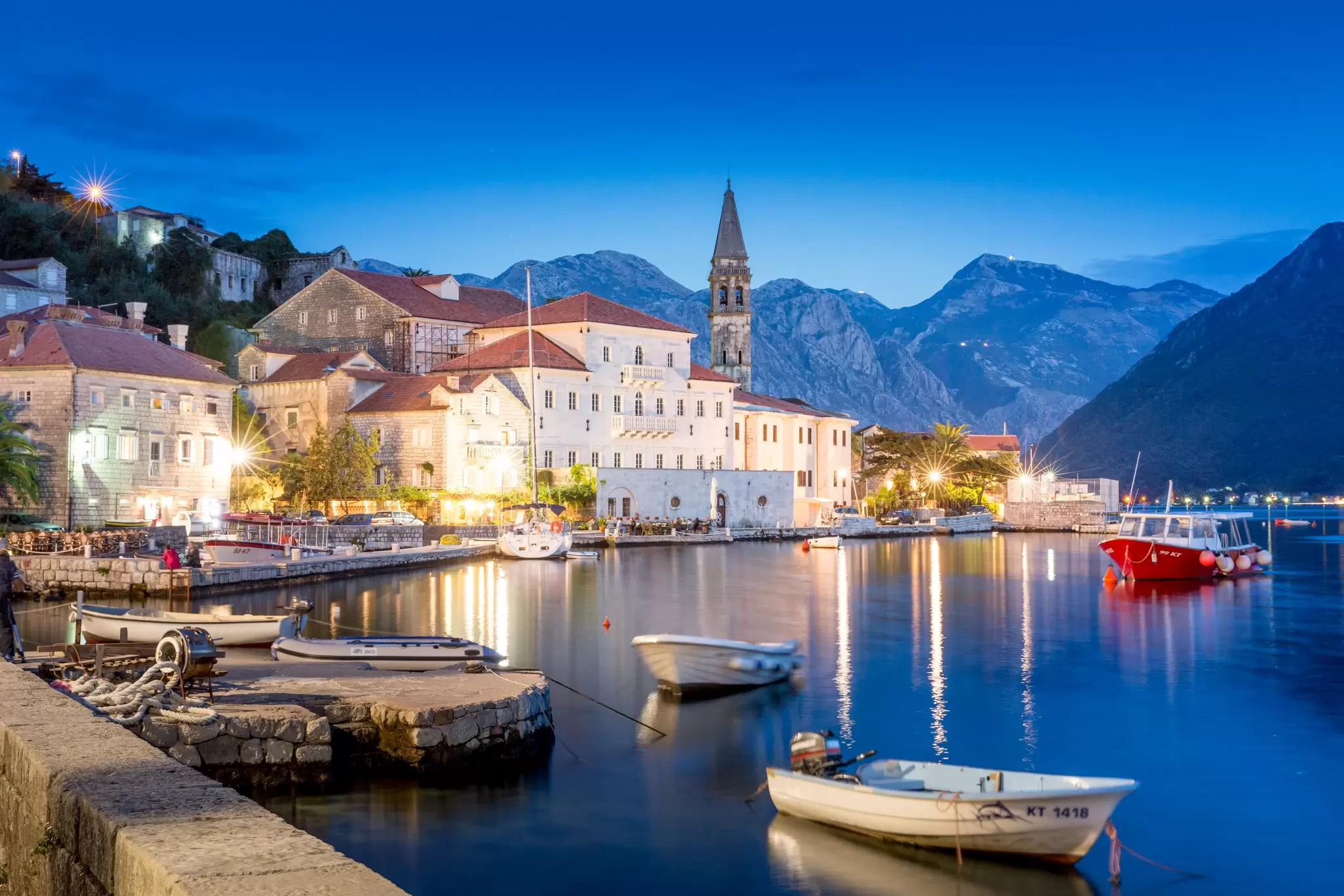 waterfront of a European town at night, with a church, small boats docked and mountains in the background