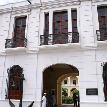 A Mexican sailor standing guard outside a naval museum entrance on a sunny day.