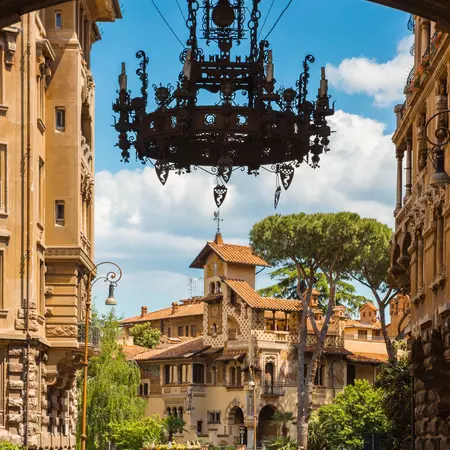 A large ornate wrought-iron chandelier that hangs under an archway of a neighborhood in Rome