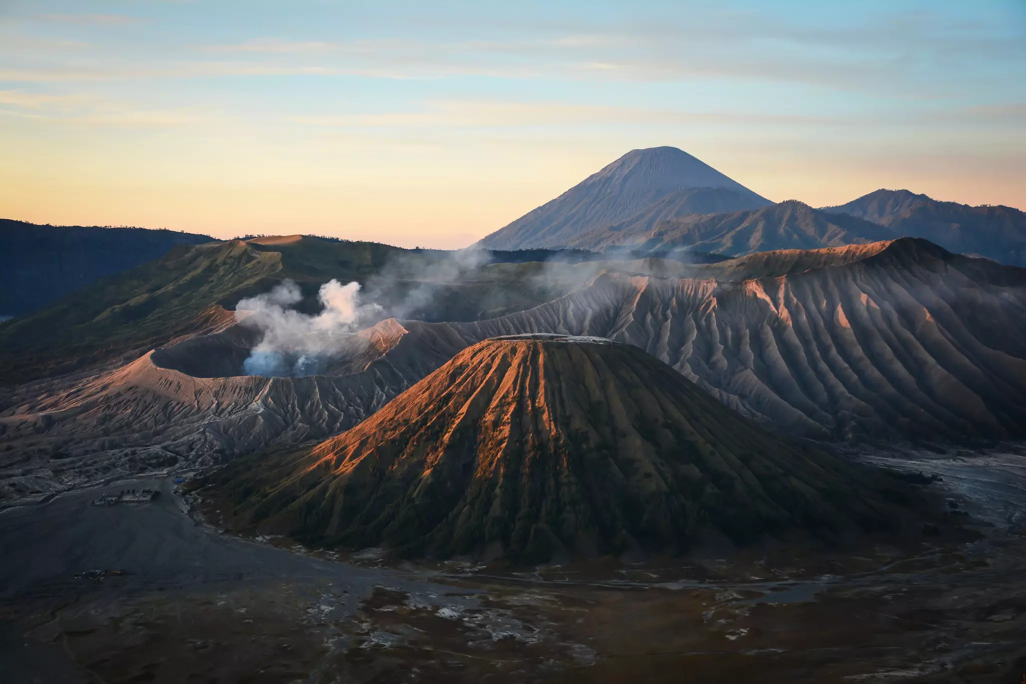 Five volcanic cones in pink light, with smoke drifting over the cone to the left.