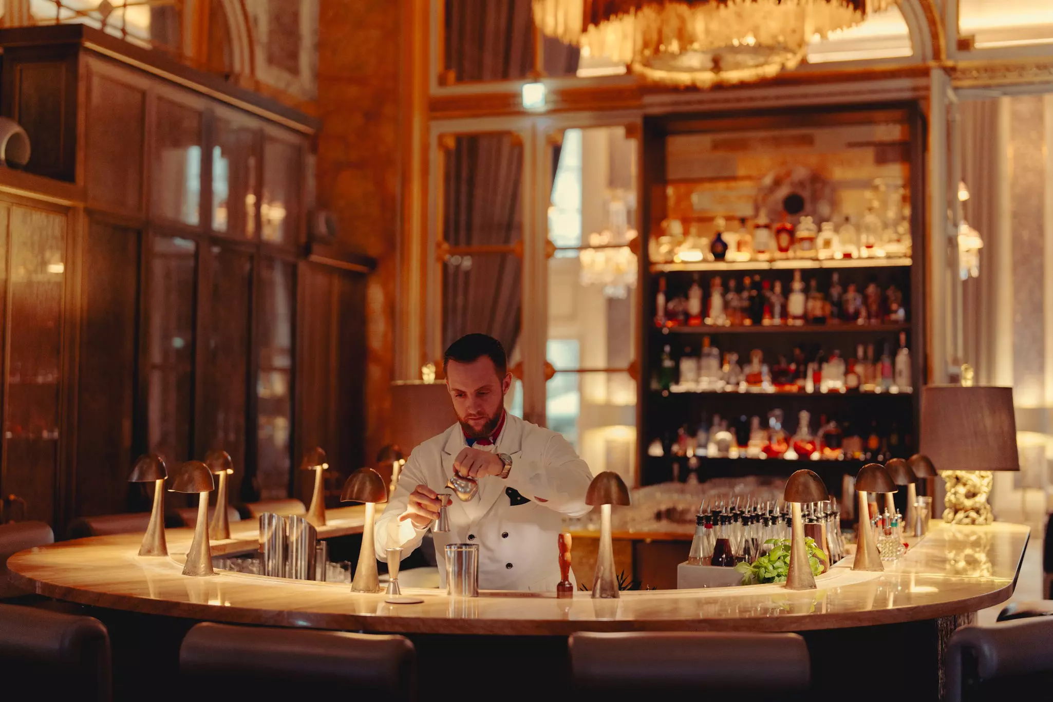 A bartender making a drink behind a grand bar stocked with many different drinks