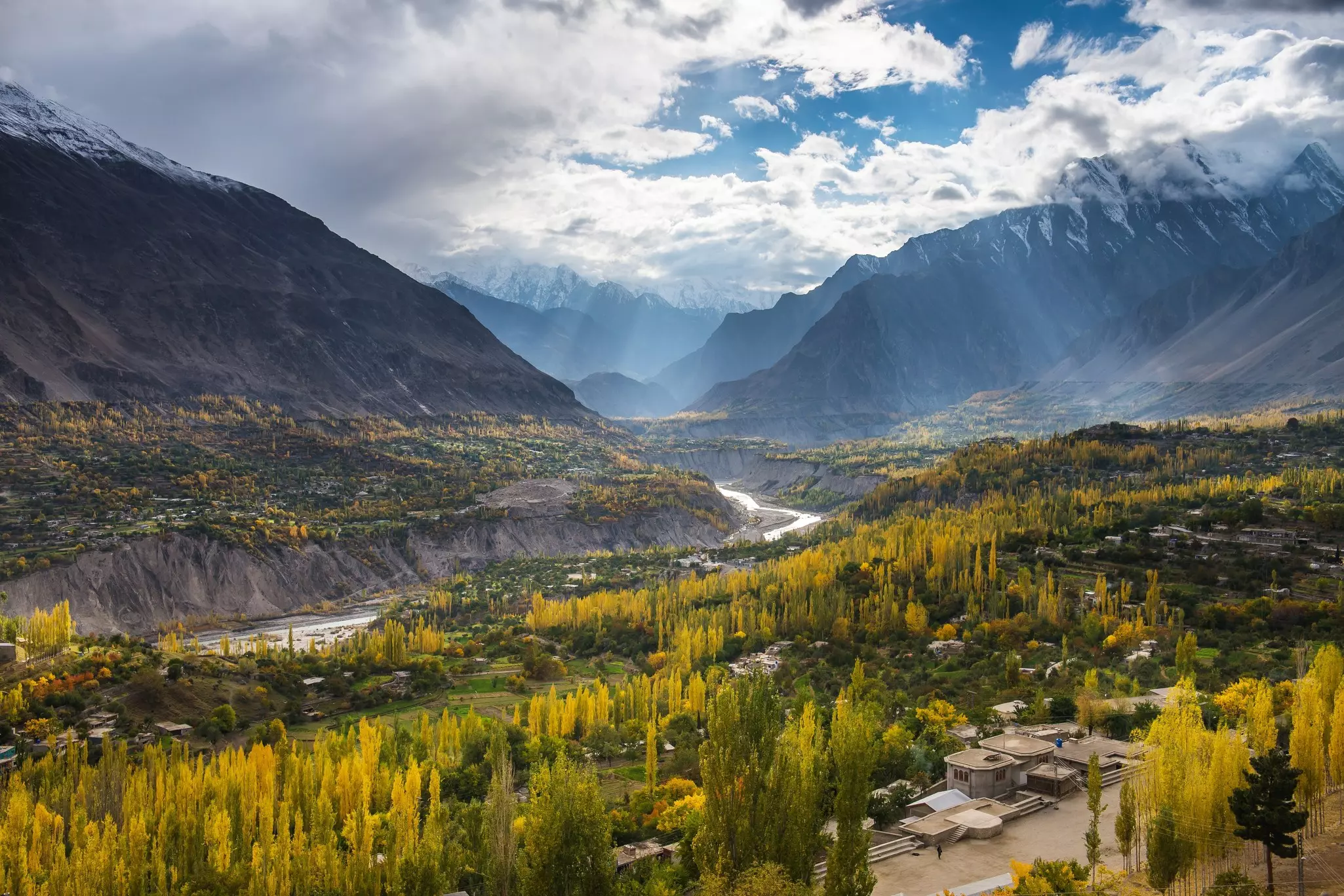 A river in Pakistan carves its way through a mountain valley cast in autumn sun; trees are turning yellow.