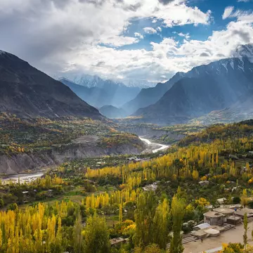 A river in Pakistan carves its way through a mountain valley cast in autumn sun; trees are turning yellow.
