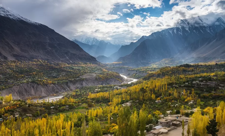 A river in Pakistan carves its way through a mountain valley cast in autumn sun; trees are turning yellow.