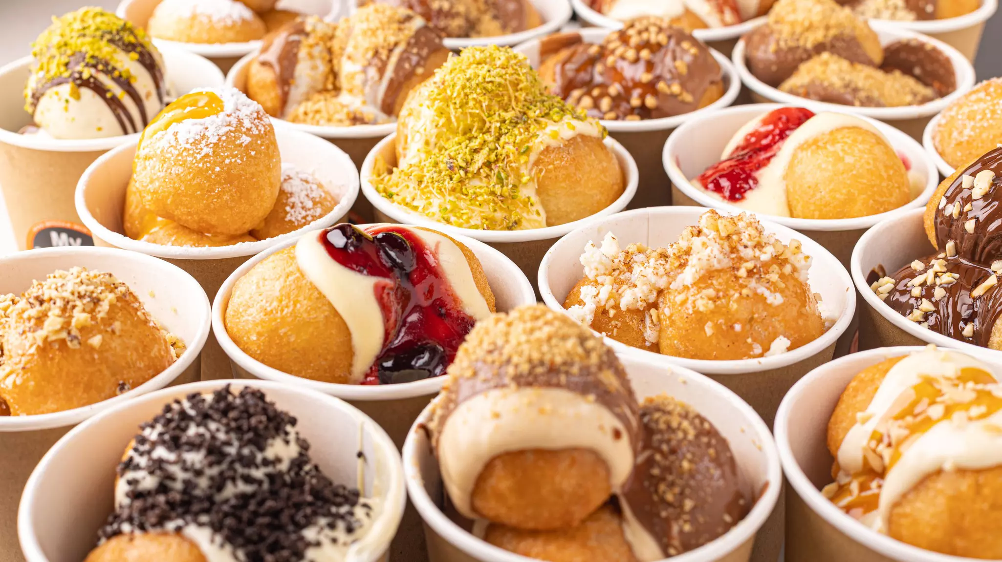 Traditional loukoumadhes doughnut balls with different toppings in cups from above-top view.