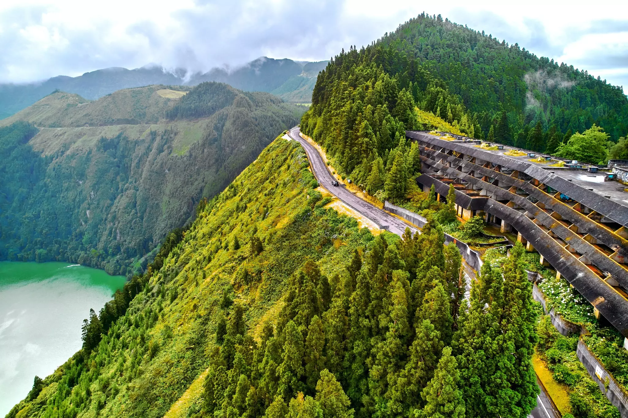 A road follows the edge of the Lagoa das Sete Cidades in São Miguel, looking over forests and green waters.