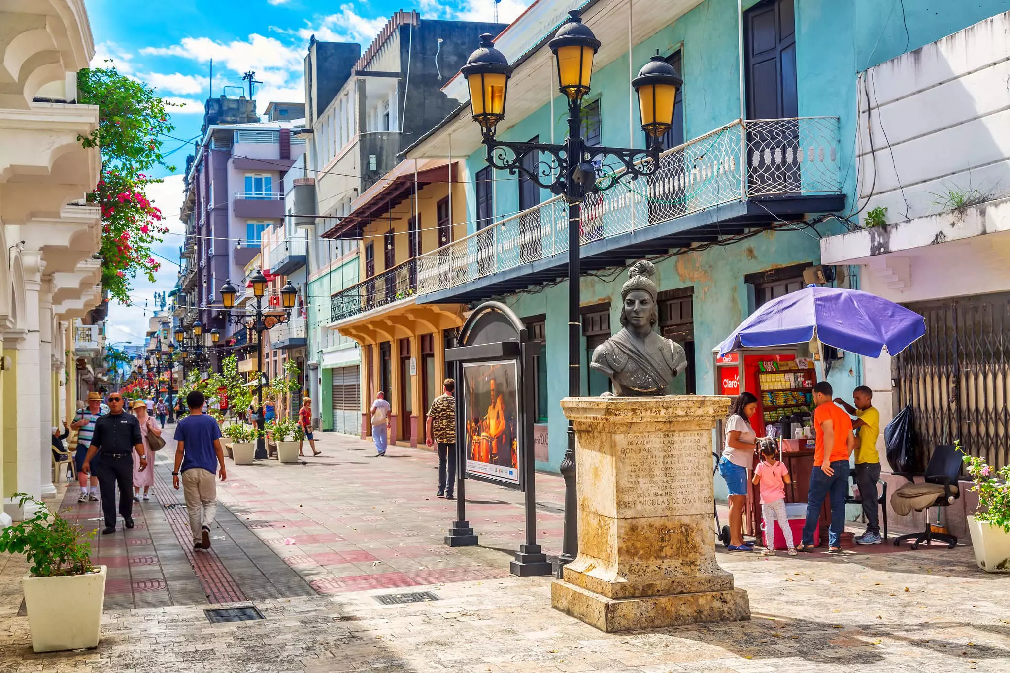 A bronze bust of a woman stands at one end of a pedestrianized street lined with historic buildings