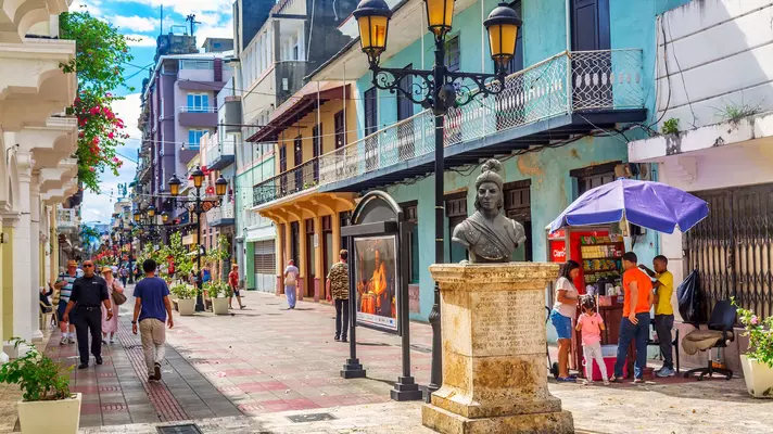 A bronze bust of a woman stands at one end of a pedestrianized street lined with historic buildings