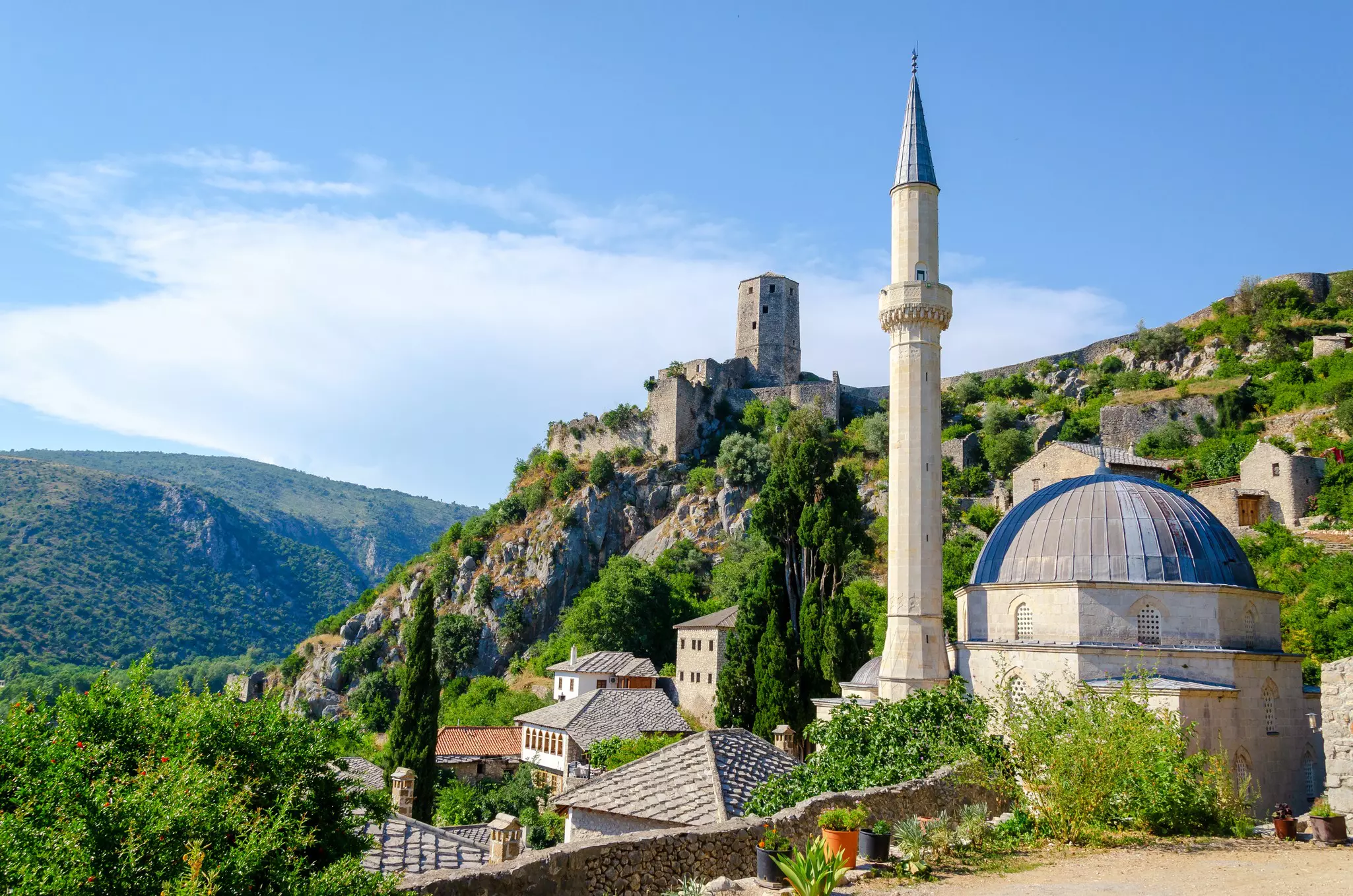 A hillside village with a castle tower and a mosque with a tall minaret.