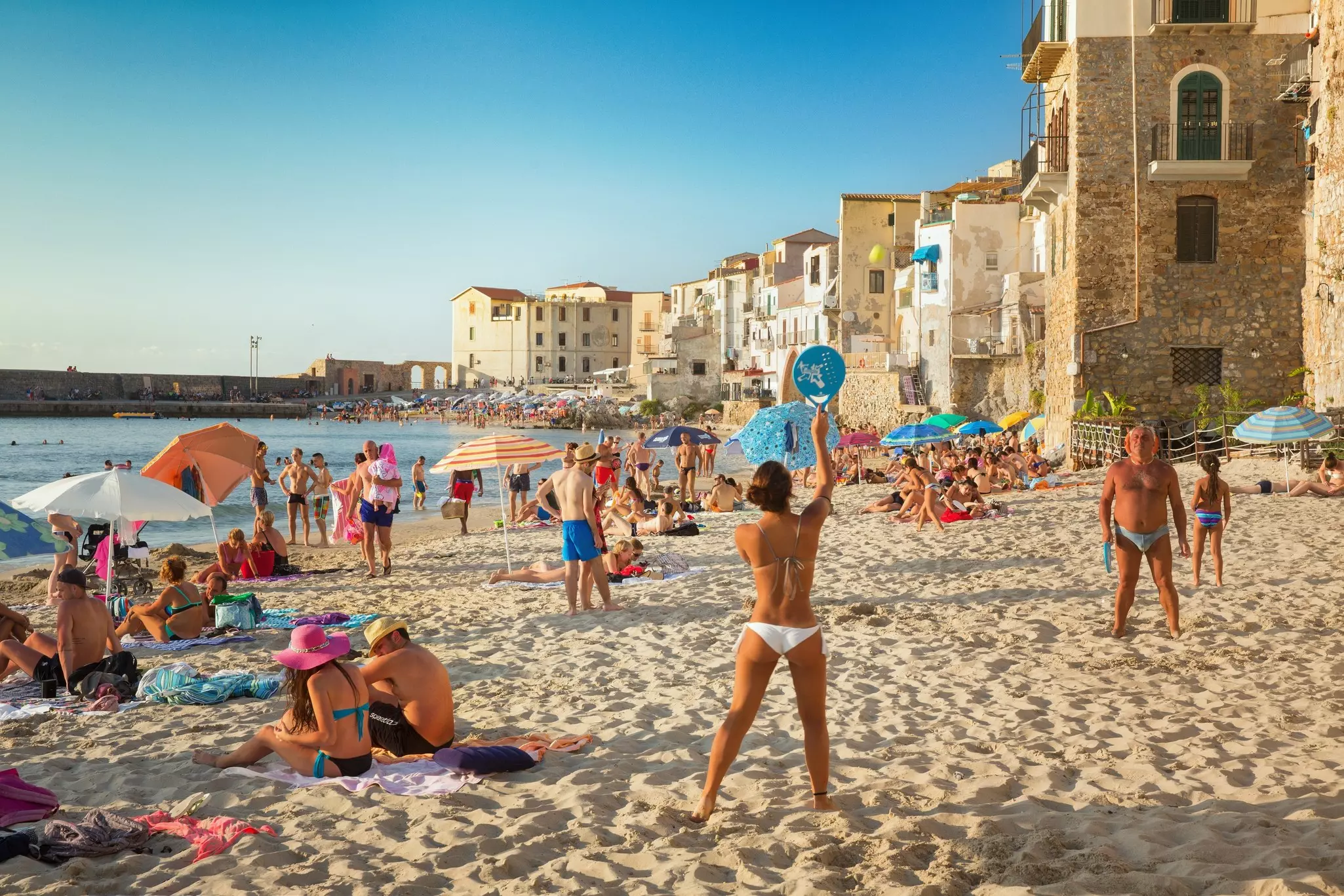 People on a sandy beach in Cefalù, Sicily, Italy.