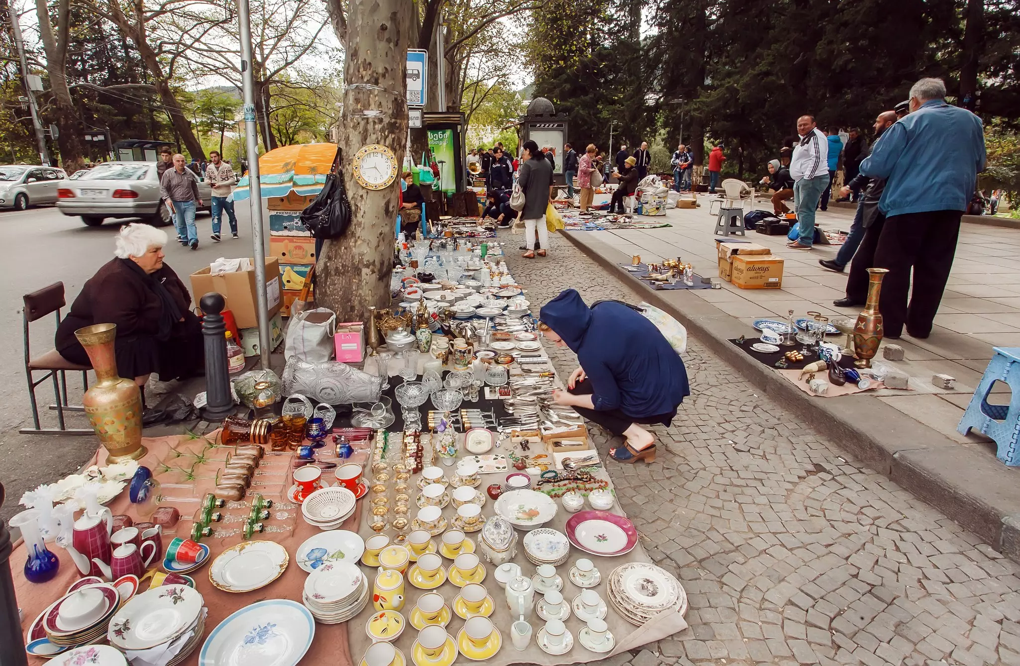 Customers at a flea market where wares are arranged on cloths on the ground along a sidewalk