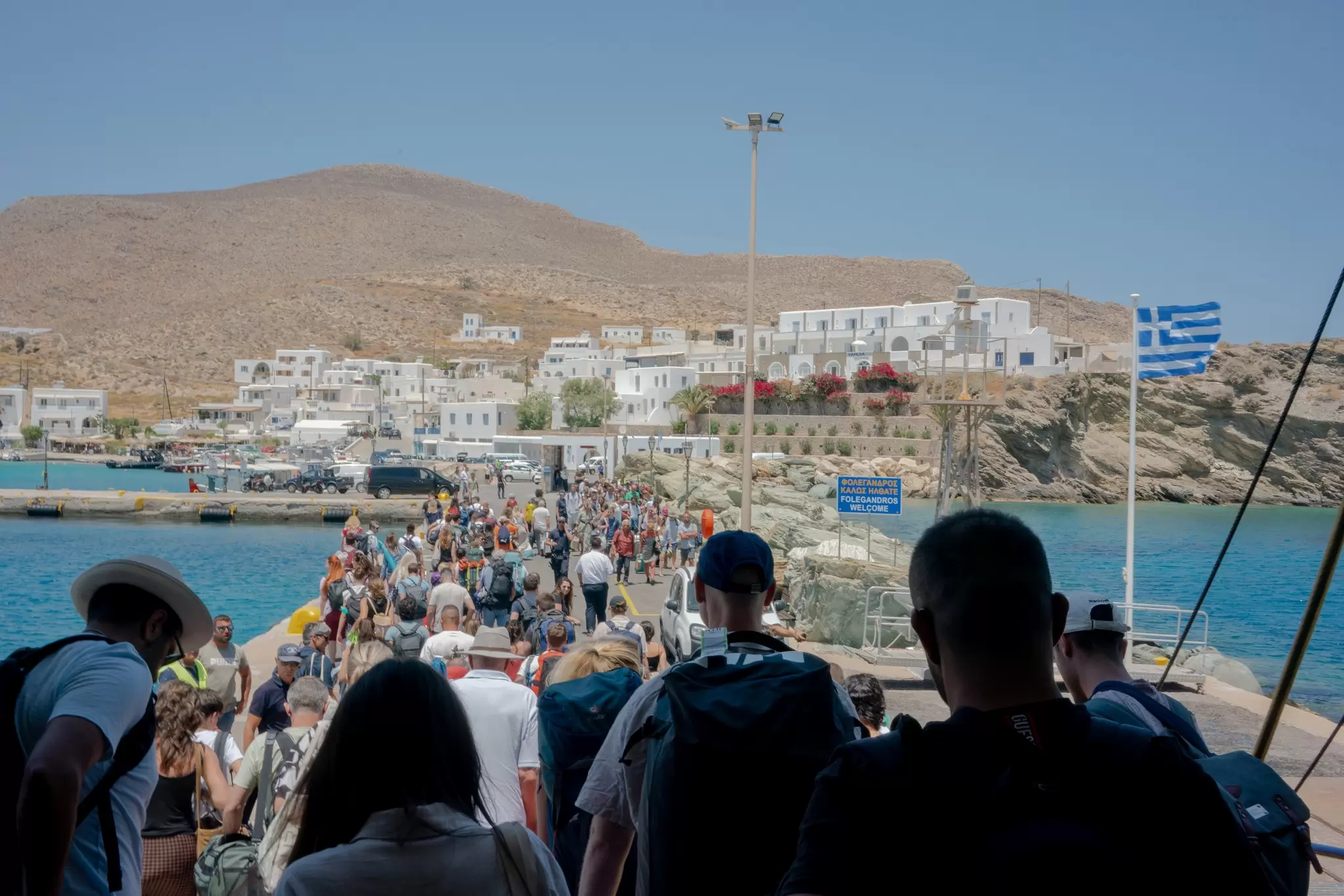 Crowds of people getting off a ferry at a small island port with a Greek flag flying next to it