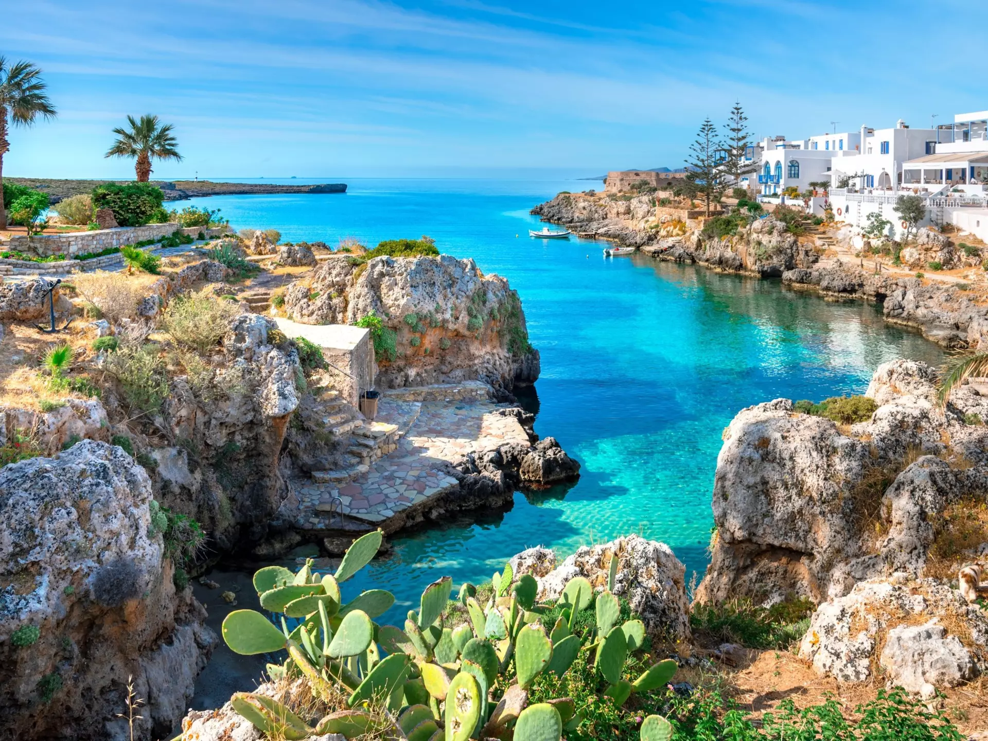 A village with white buildings is seen at the edge of a sea inlet with bright blue water.