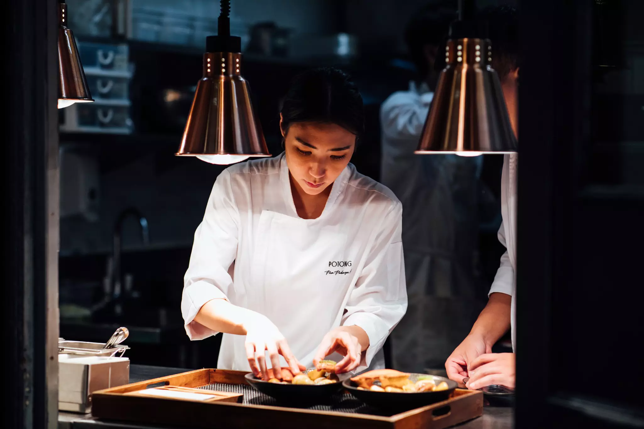 A female chef is seen plating food in the kitchen of a restaurant.