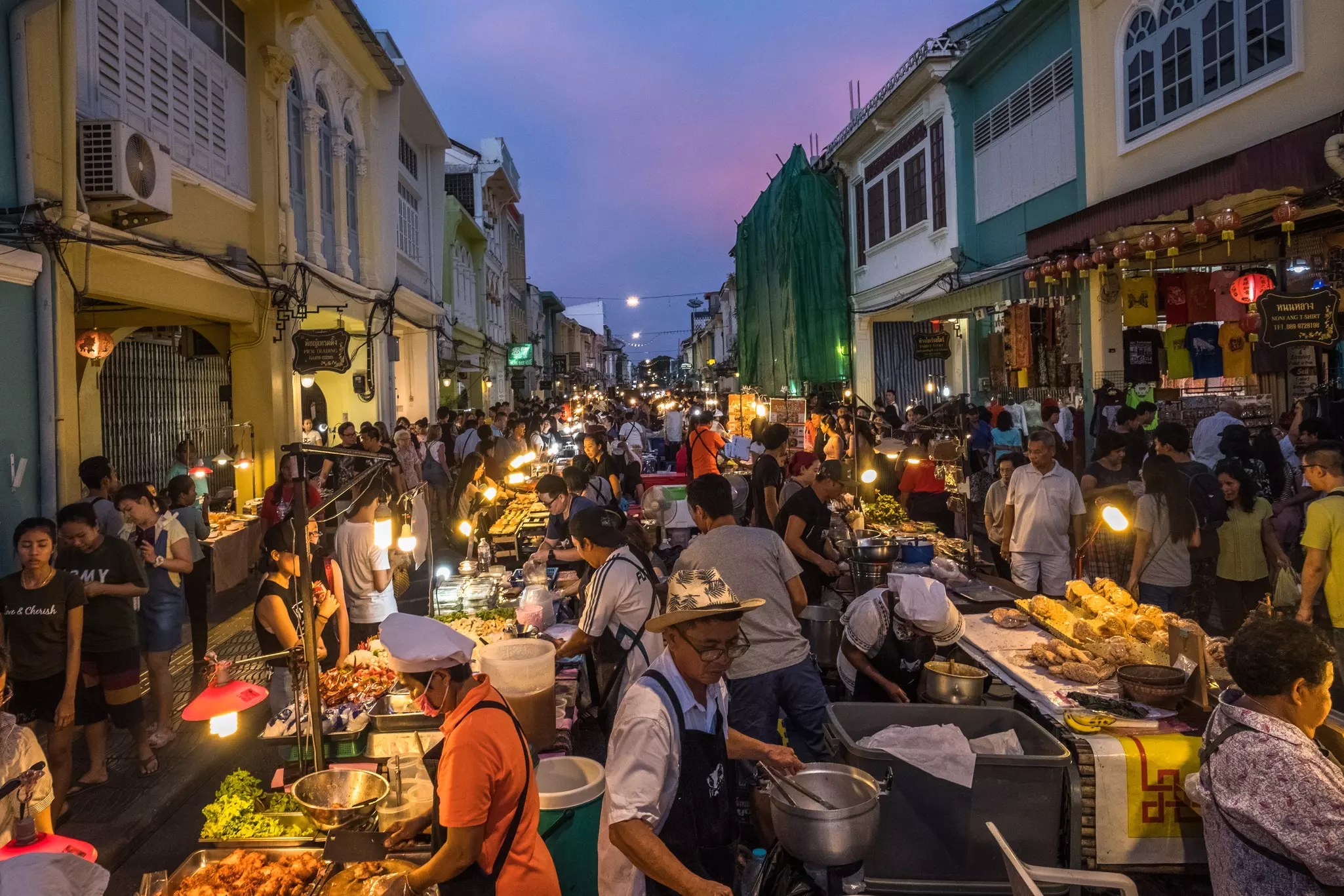 A street food market at dusk with a crowd of locals and tourists