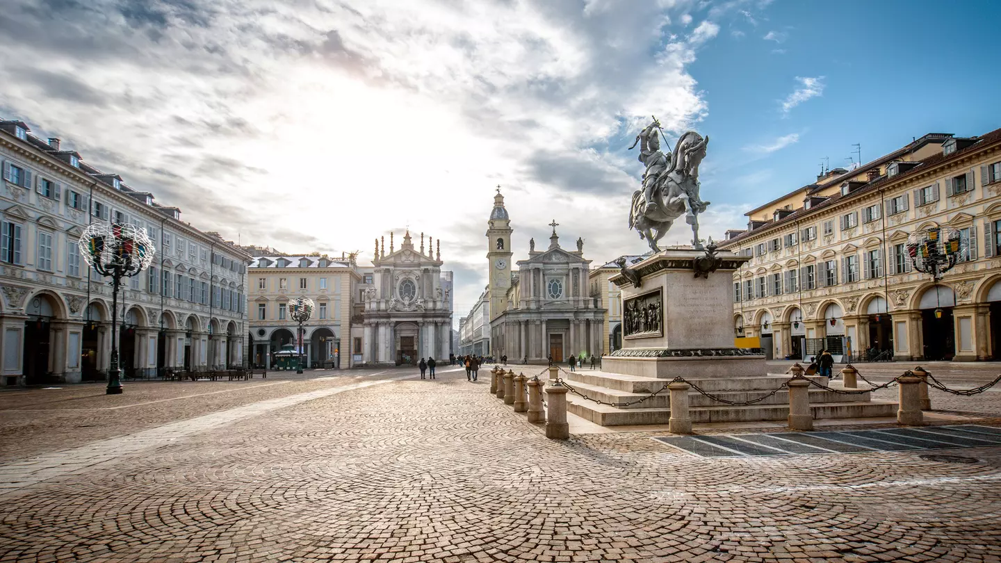 People walk through a large elegant cobbled square with two churches at one end