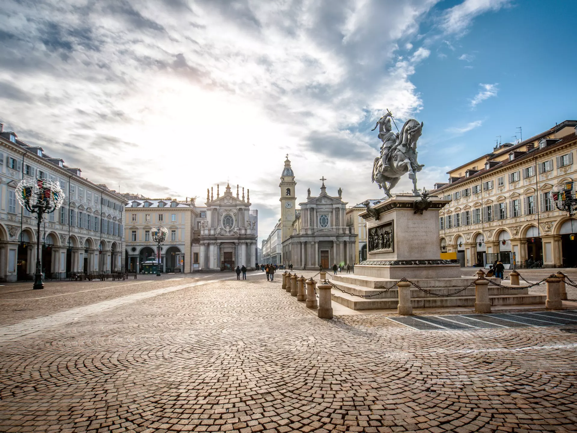 People walk through a large elegant cobbled square with two churches at one end