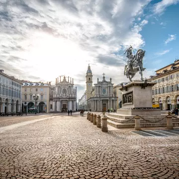 People walk through a large elegant cobbled square with two churches at one end