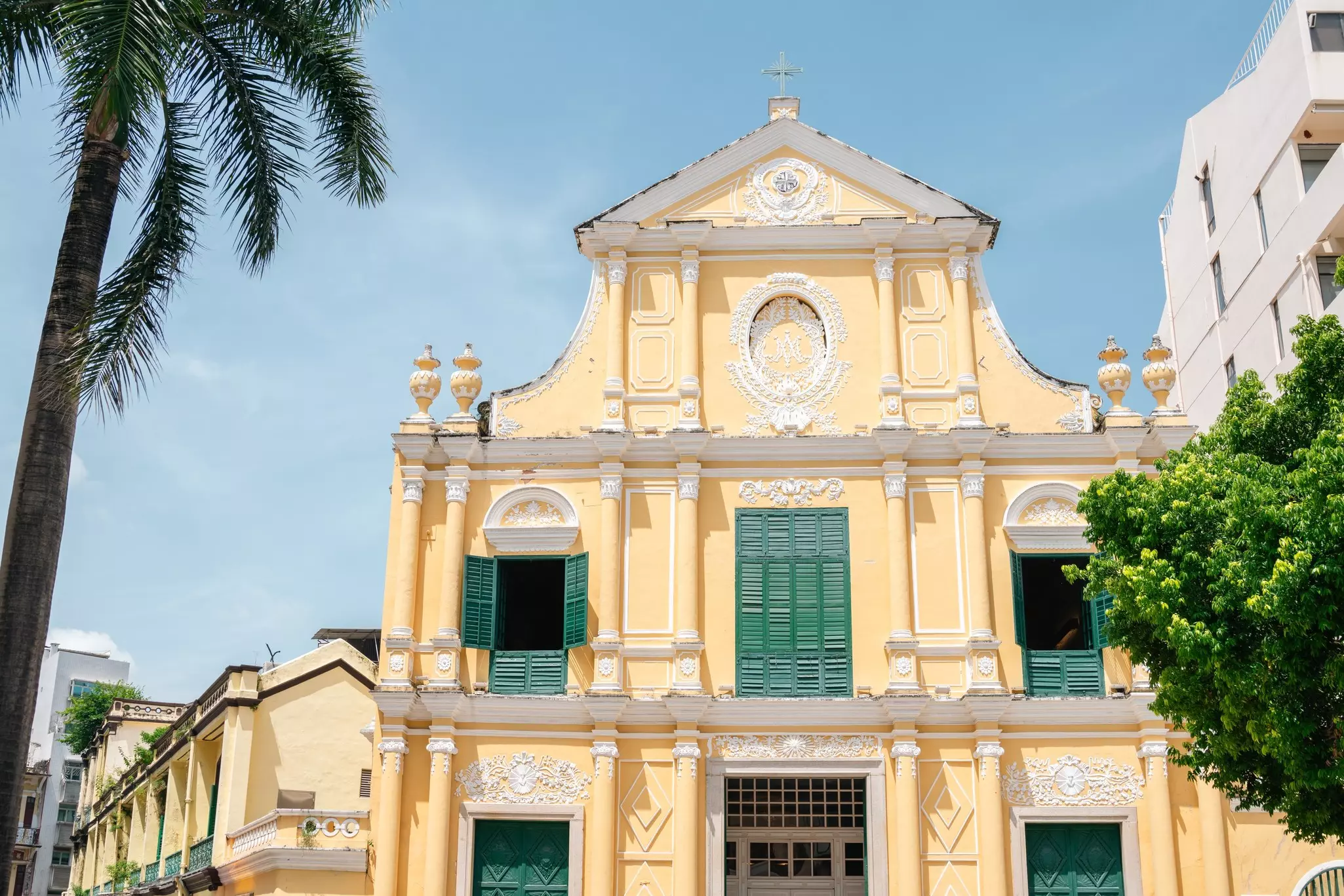 The buttery yellow facade of St. Dominic's Church with green shutters on it and green trees nearby