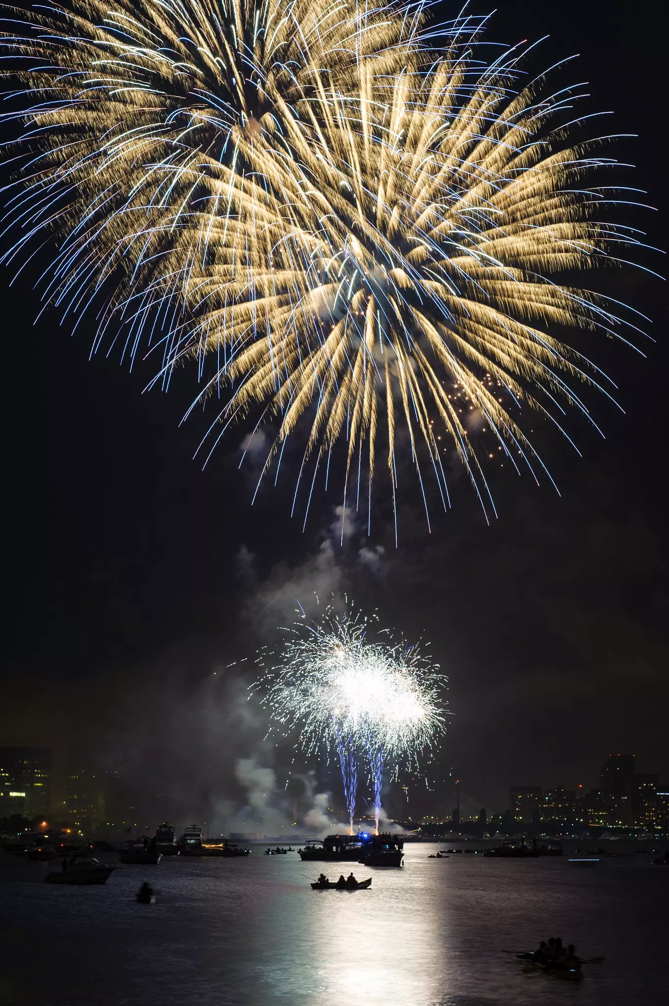 Blue, gold and white fireworks in Boston over the a river with kayaks and boats in the water