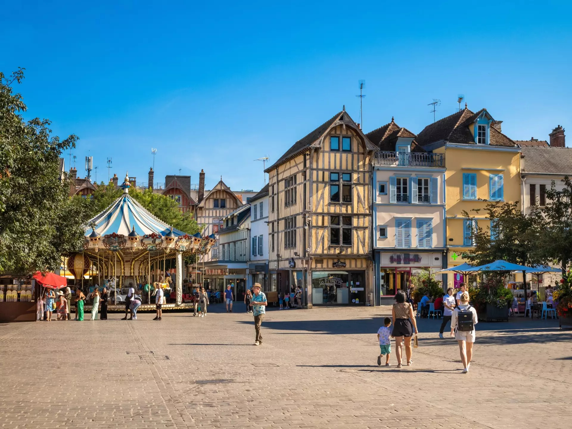 People wander through a square lined with medieval buildings and a classic carousel
