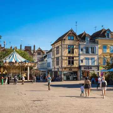 People wander through a square lined with medieval buildings and a classic carousel