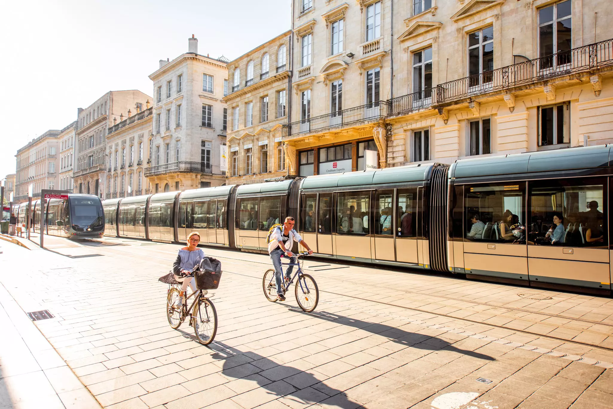 Street view with people two riding bicycles in the morning in front of modern trams in the city of Bordeaux, France