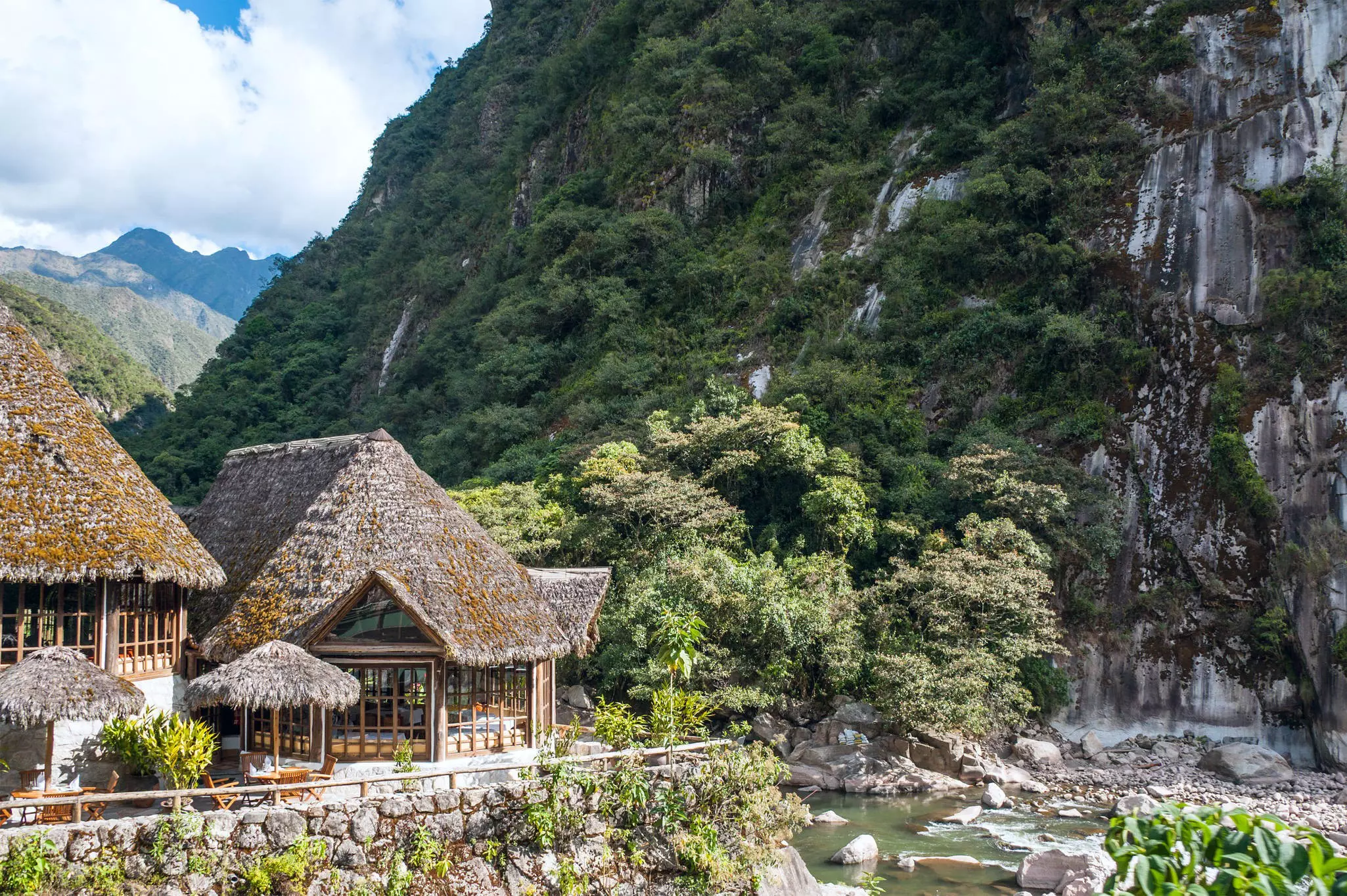 Two buildings at the foot of a green mountain.