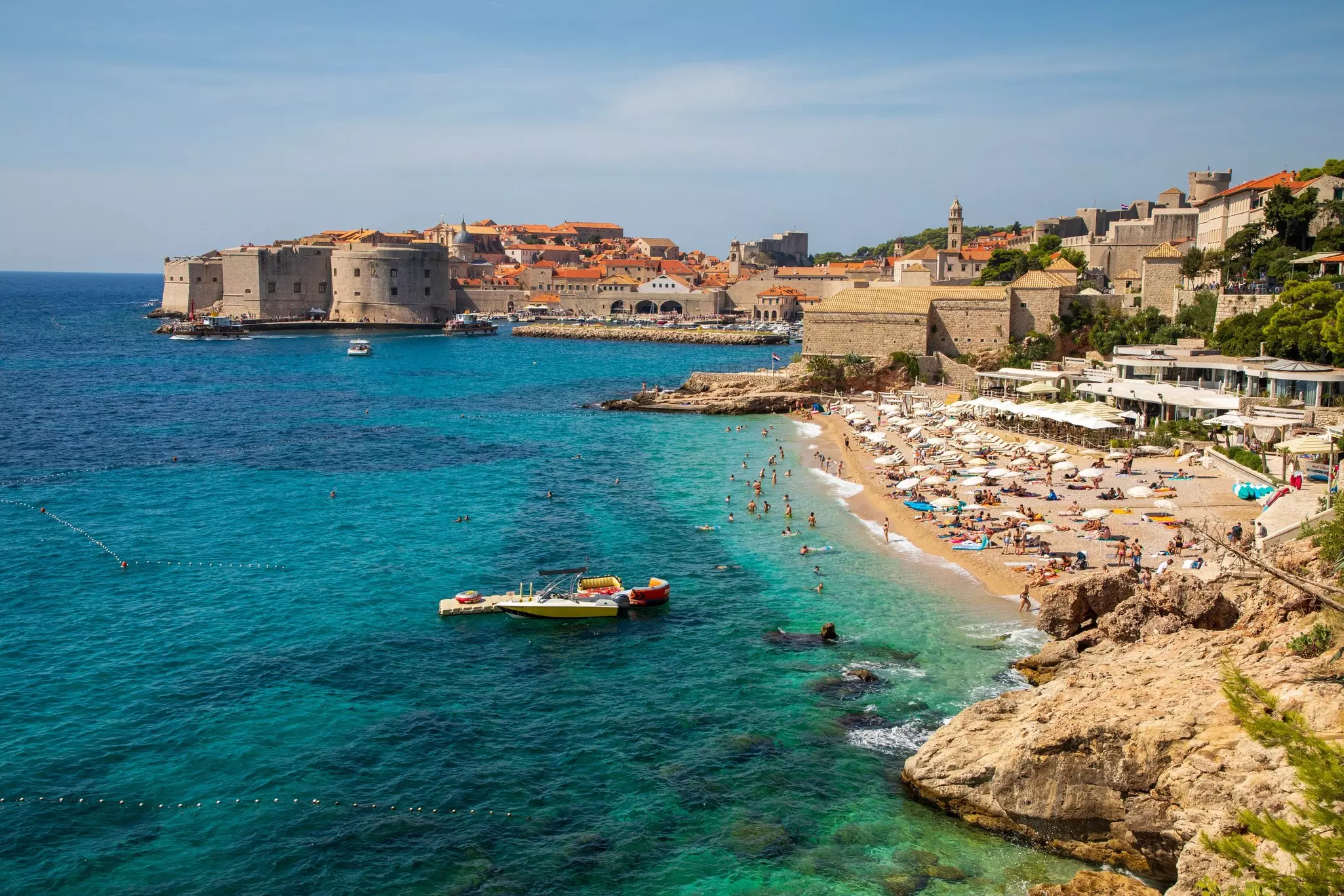 Old town Dubrovnik and Banje beach at its feet. People on the sand at the end of the afternoon. 