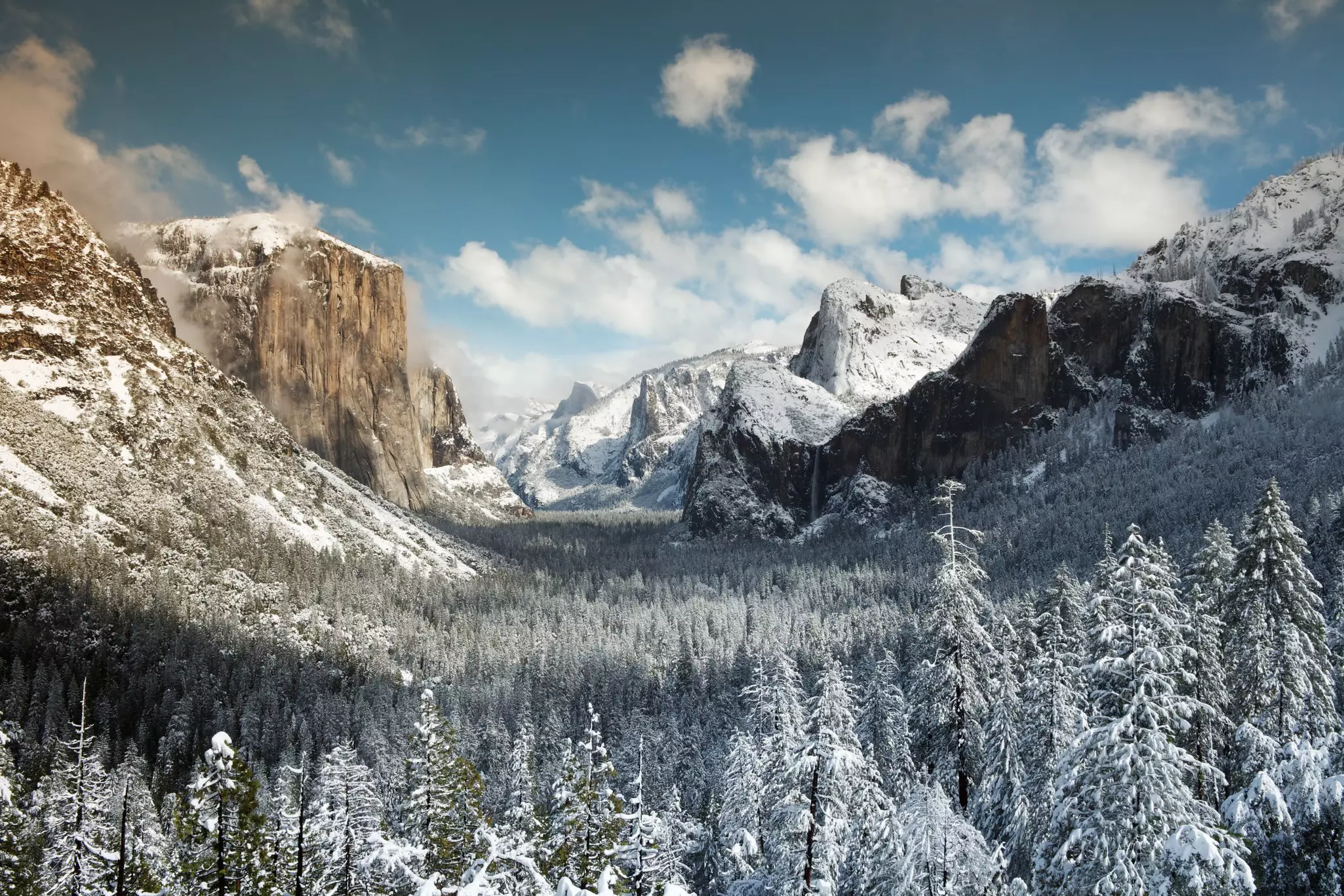 A snowy valley landscape with tall rocks and mountains either side.
