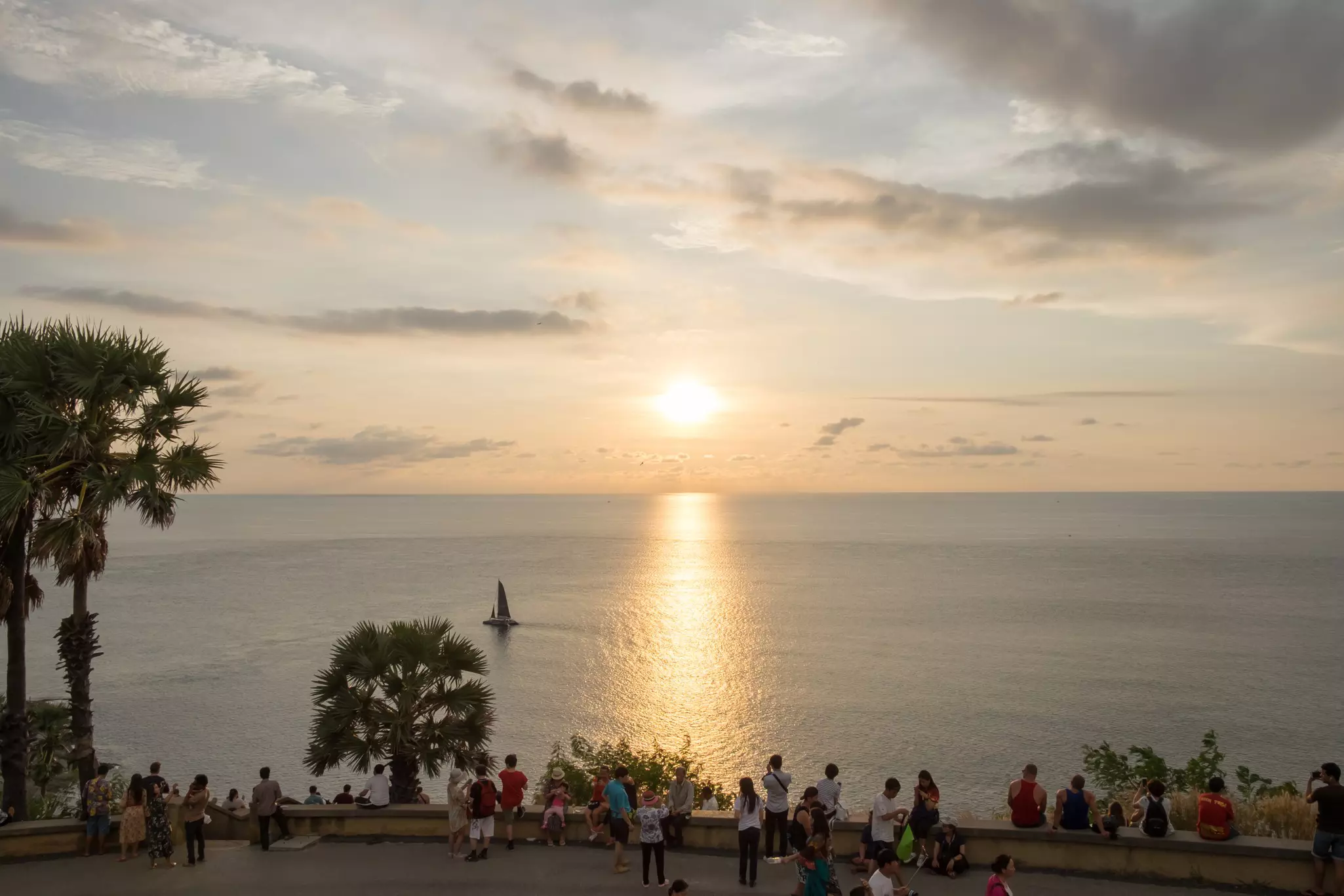 People gather along a road on a coast to watch the sun set over the sea.