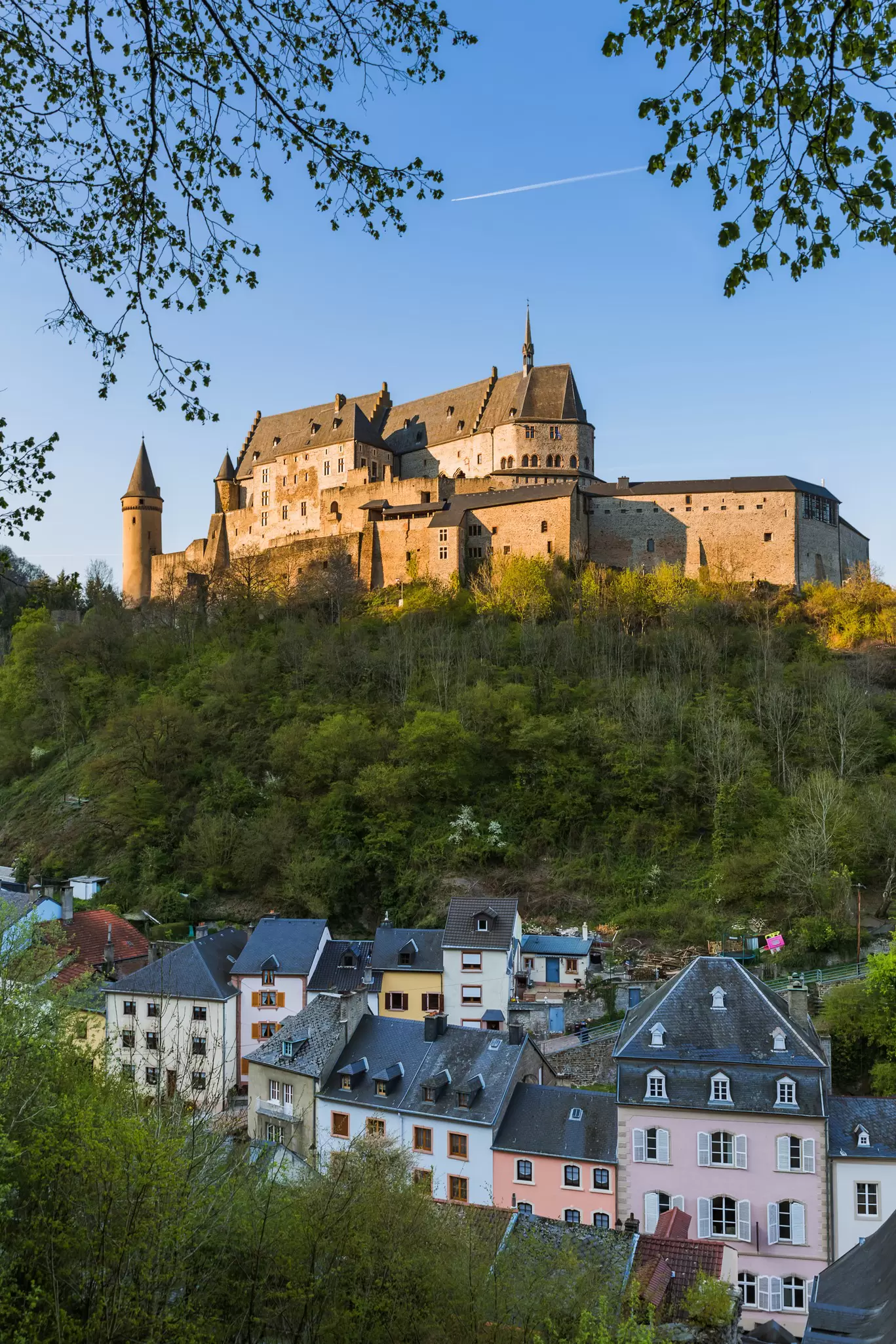 A large golden stone castle on a green hill; a town of multicolored buildings is below.