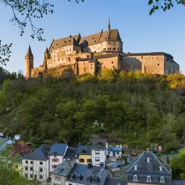 A large golden stone castle on a green hill; a town of multicolored buildings is below.