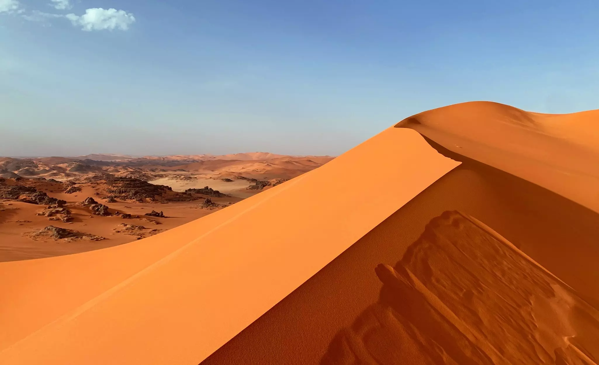 A large dune of red sand above a rocky plateau in Algeria.