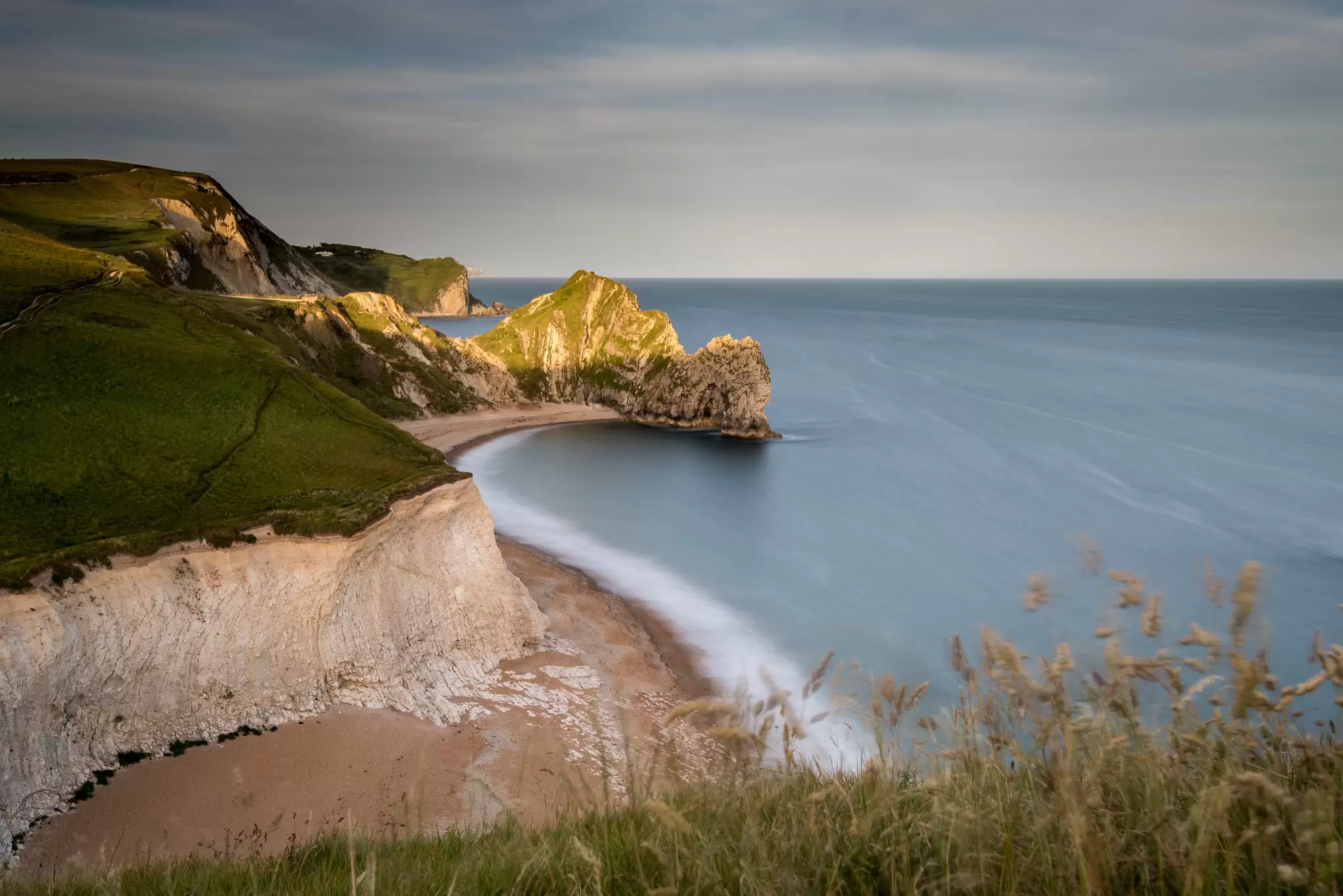Undulating cliffs leading down to a sandy and shingle beach, with a huge stone archway at one end